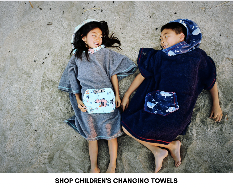 Two kids laying in the sand, wearing our children's changing towels.